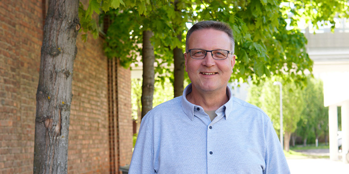 Petteri Asikainen seisoo ja hymyilee kohti kameraa.