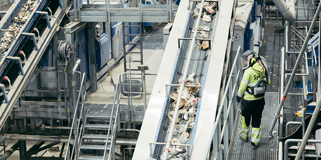 Jätteiden lajittelulaitoksella operaattori kävelee ja tarkkailee linjastoa.