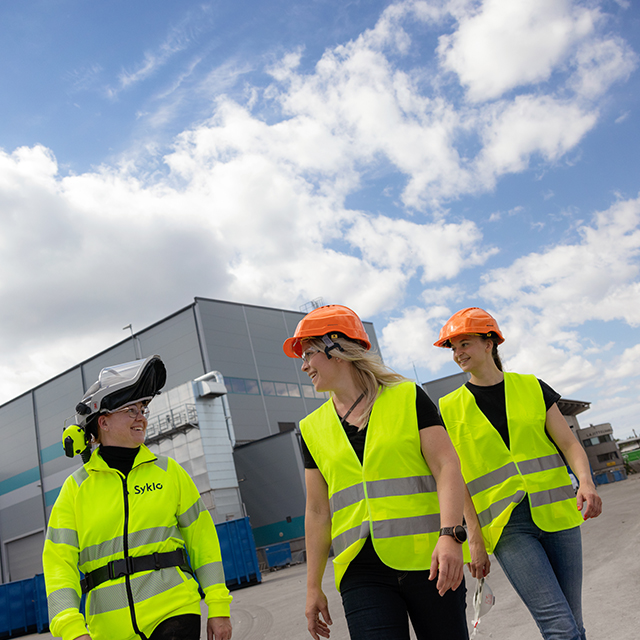 Kolme Syklon työntekijää kävelee lajittelulaitoksen pihalla.