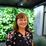 Päivi Pälve seisoo hymyille toimiston viherseinän edessä.