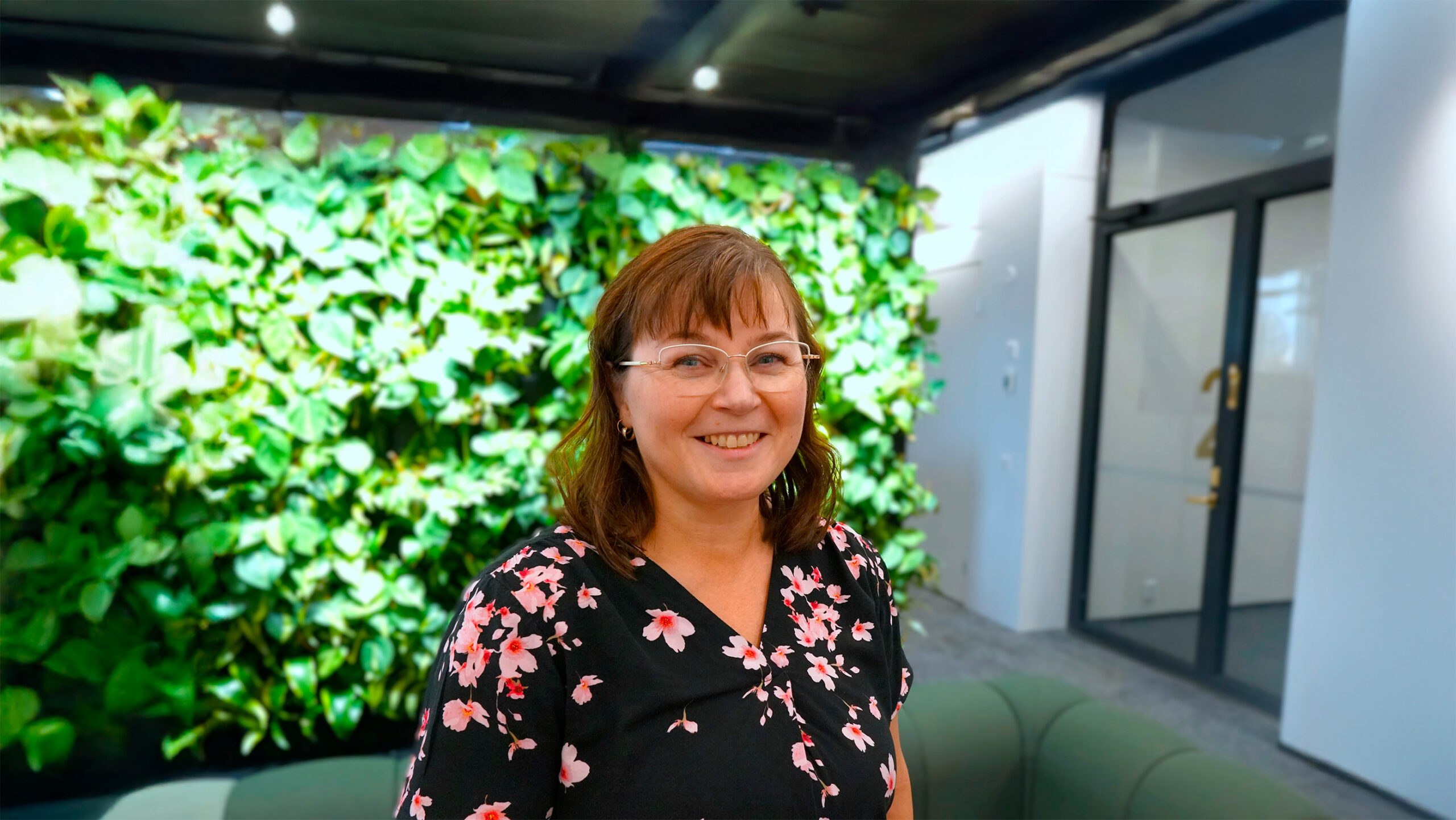 Päivi Pälve seisoo hymyillen toimiston viherseinän edessä.