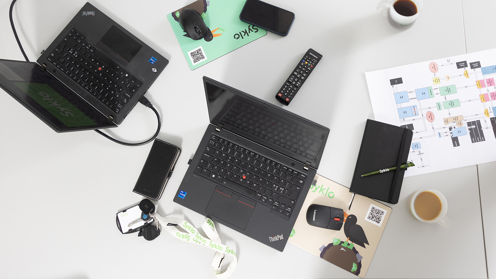 Kaksi kannettavaa tietokonetta ja Syklon logoilla koristeltuja toimistotarvikkeita suoraan yläpuolelta kuvattuna.